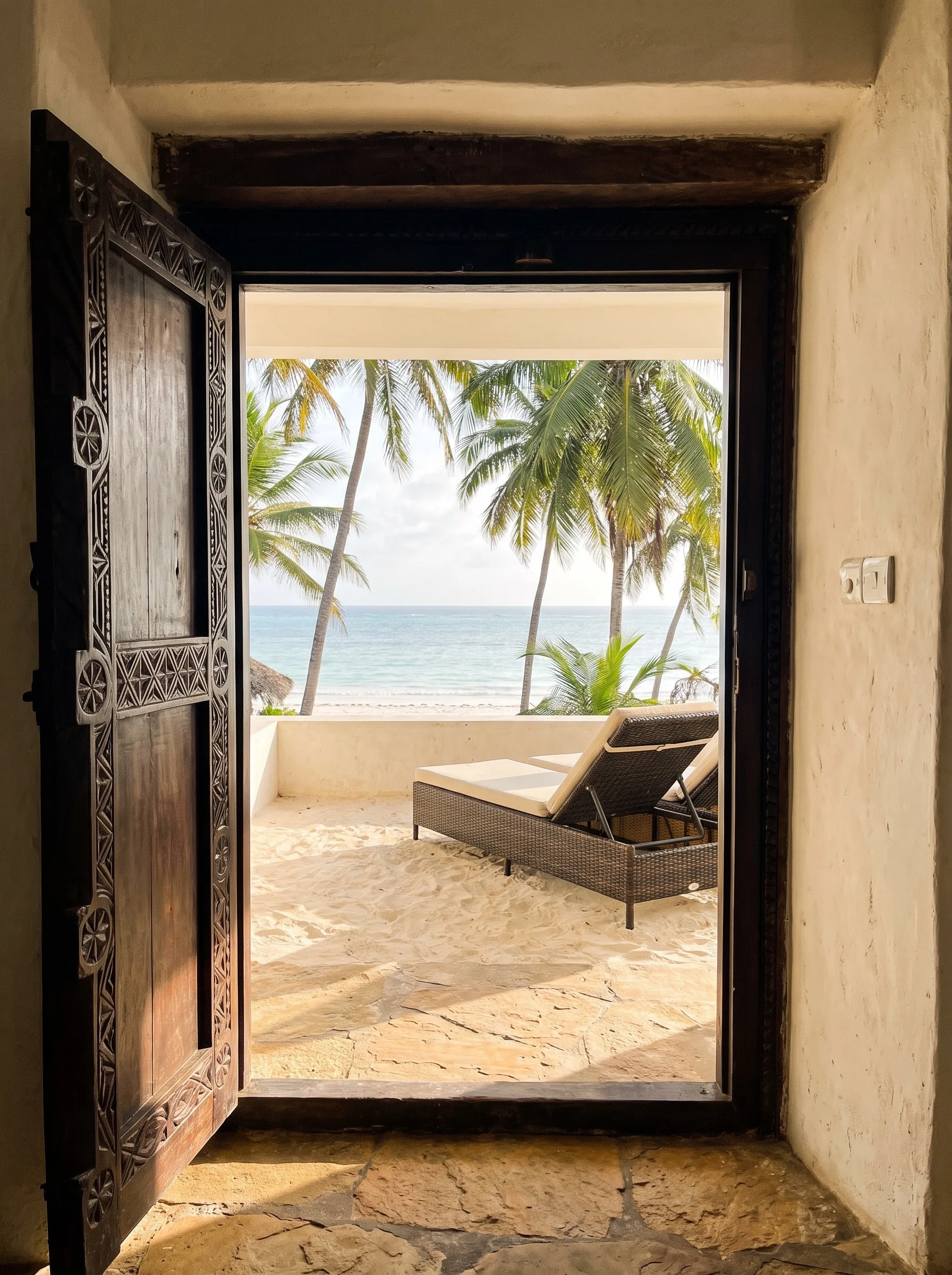 An arched doorway opening onto a sunny terrace with a lounger and palms