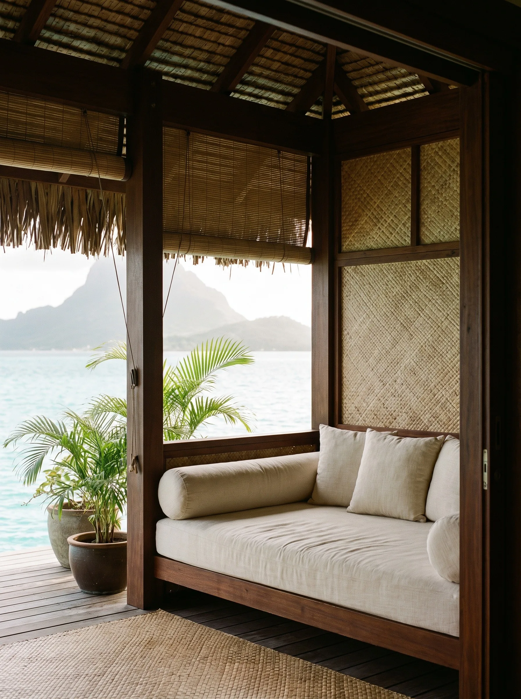 A cushioned daybed in a thatched pavilion looking out to a lagoon and mountains